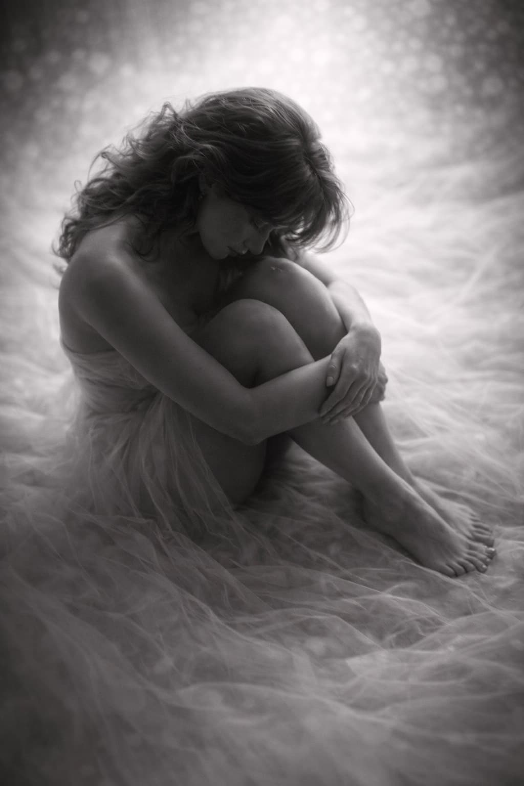 Photographie boudoir artistique en noir et blanc d’une femme assise, les bras entourant ses jambes, dans une ambiance intime au studio de Tourcoing.